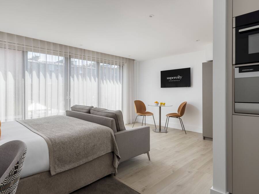 A modern bedroom with a bed, a sofa, a TV, and a dining area with chairs.