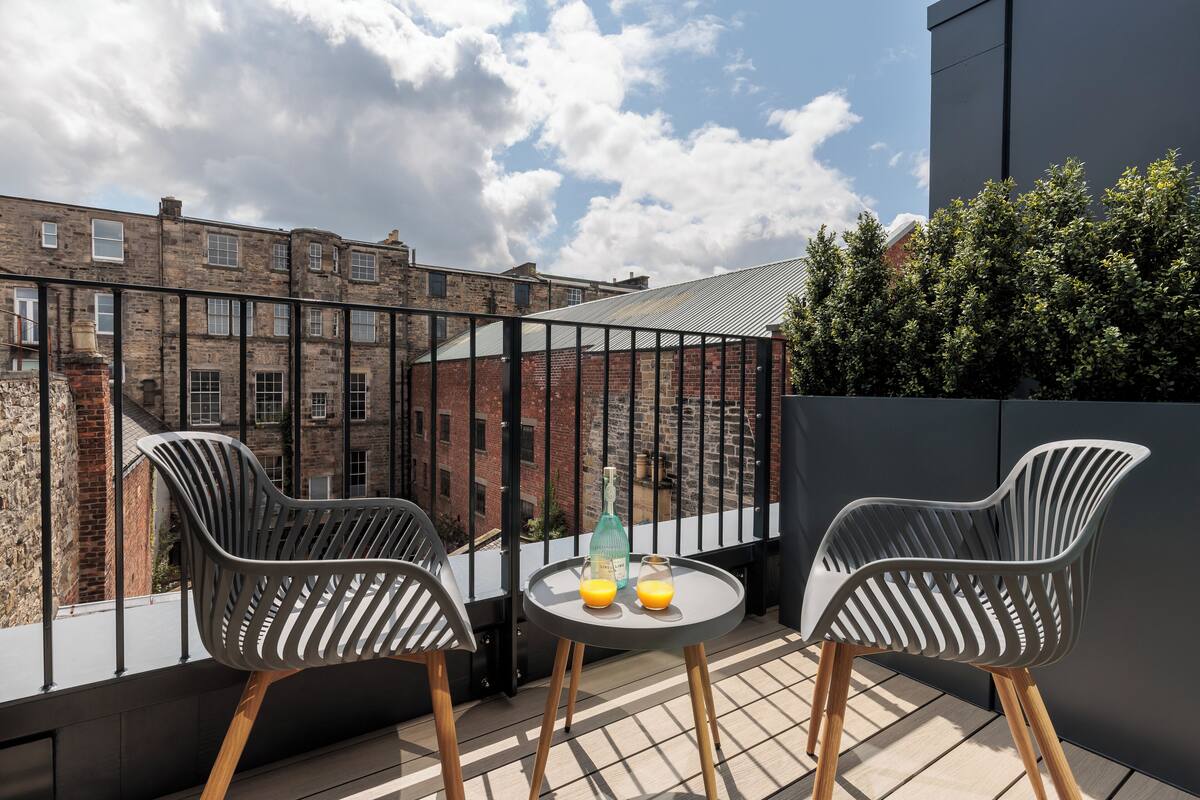 A balcony with two modern chairs, a small table, and two glasses of orange juice.