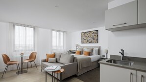 A modern hotel room with a bed, a sofa, a dining table with chairs, a kitchen area, and large windows. - Forth House by Supercity Aparthotels (Edinburgh)