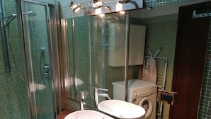 Ett badrum med en dusch som är avskärmad med glasväggar, en dubbel tvättställ och en tvättmaskin.