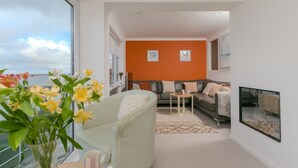 A modern living room with a sofa, a coffee table, and a view of the sky through a large window.