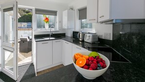 A modern kitchen with white cabinets, a black countertop, and a bowl of fruit.