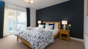 A bedroom with a large bed, two bedside tables with lamps, a view through a sliding door, and a dark accent wall.