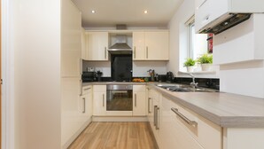 A modern kitchen with light-colored cabinets, a stainless steel range hood, and a wooden countertop.