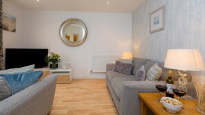 A modern living room with a sofa, a coffee table with a bowl of nuts, a lamp, and two wine glasses.