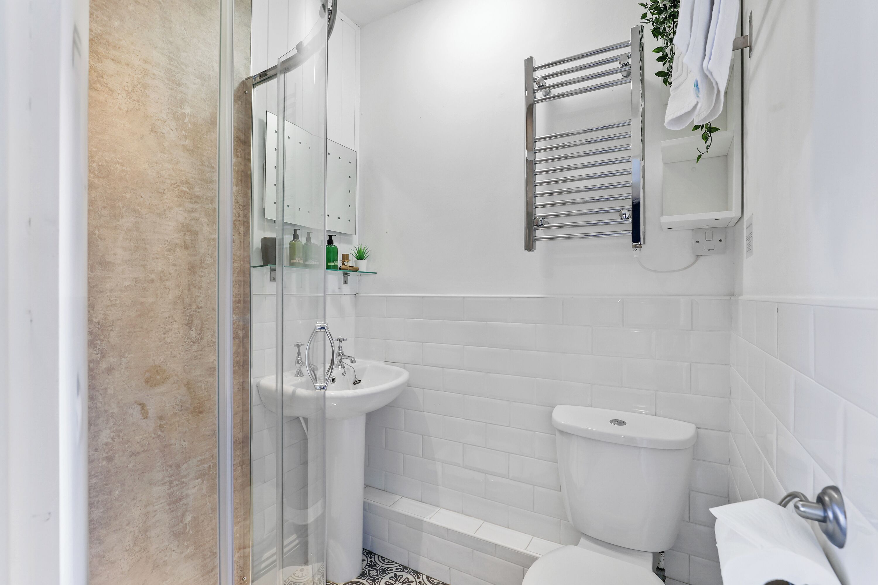 Une salle de bain moderne avec une douche à parois de verre, un lavabo sur colonne, des toilettes et un porte-serviettes agrémenté d’une plante.