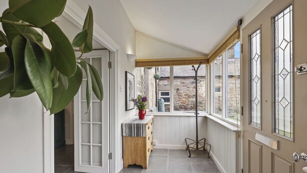 A hallway with a wooden bench, a potted plant, and a view of the outside. - Wyndgrove House - North East Escapes (Seahouses)