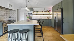 A modern kitchen with a central island, bar stools, a stainless steel refrigerator, and a microwave. - Wyndgrove House - North East Escapes (Seahouses)