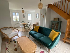 A living room with a teal sofa, wicker chairs, a small table, and a staircase. - Charming house in Groix (Groix)