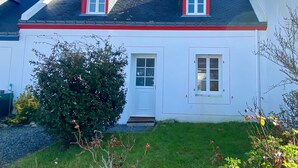 Uma casa de dois andares com telhado vermelho, fachada branca e duas janelas no andar superior.