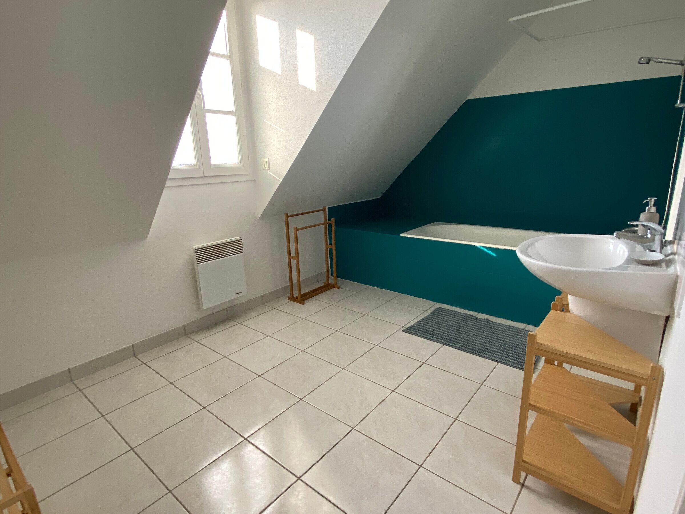 A modern bathroom with a sloped ceiling, a bathtub, a sink, and a window.