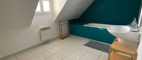 A modern bathroom with a sloped ceiling, a bathtub, a sink, and a window.