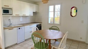 Cozinha com armários brancos, micro-ondas, pia e fogão. Há uma janela com vista para árvores e um espelho na parede.