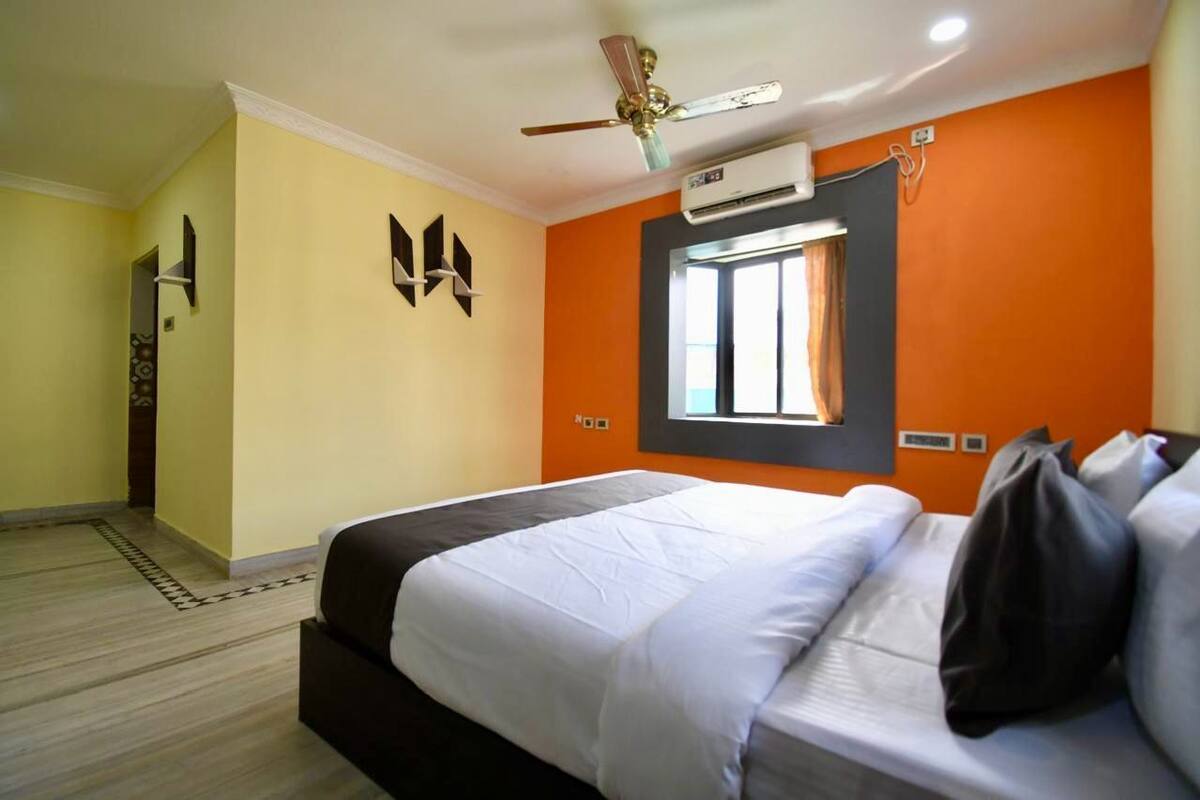 A hotel room with a bed, a ceiling fan, an air conditioning unit, and a window with curtains.