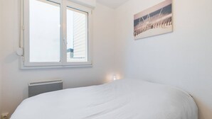 Une chambre avec un grand lit, une fenêtre avec des stores, un radiateur et un tableau accroché au mur.