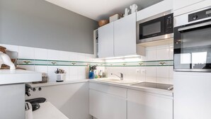 A modern kitchen with white cabinets, a microwave, an oven, and a sink. - Apartment with Terrace and Parking in Le Touquet (Le Touquet-Paris-Plage)