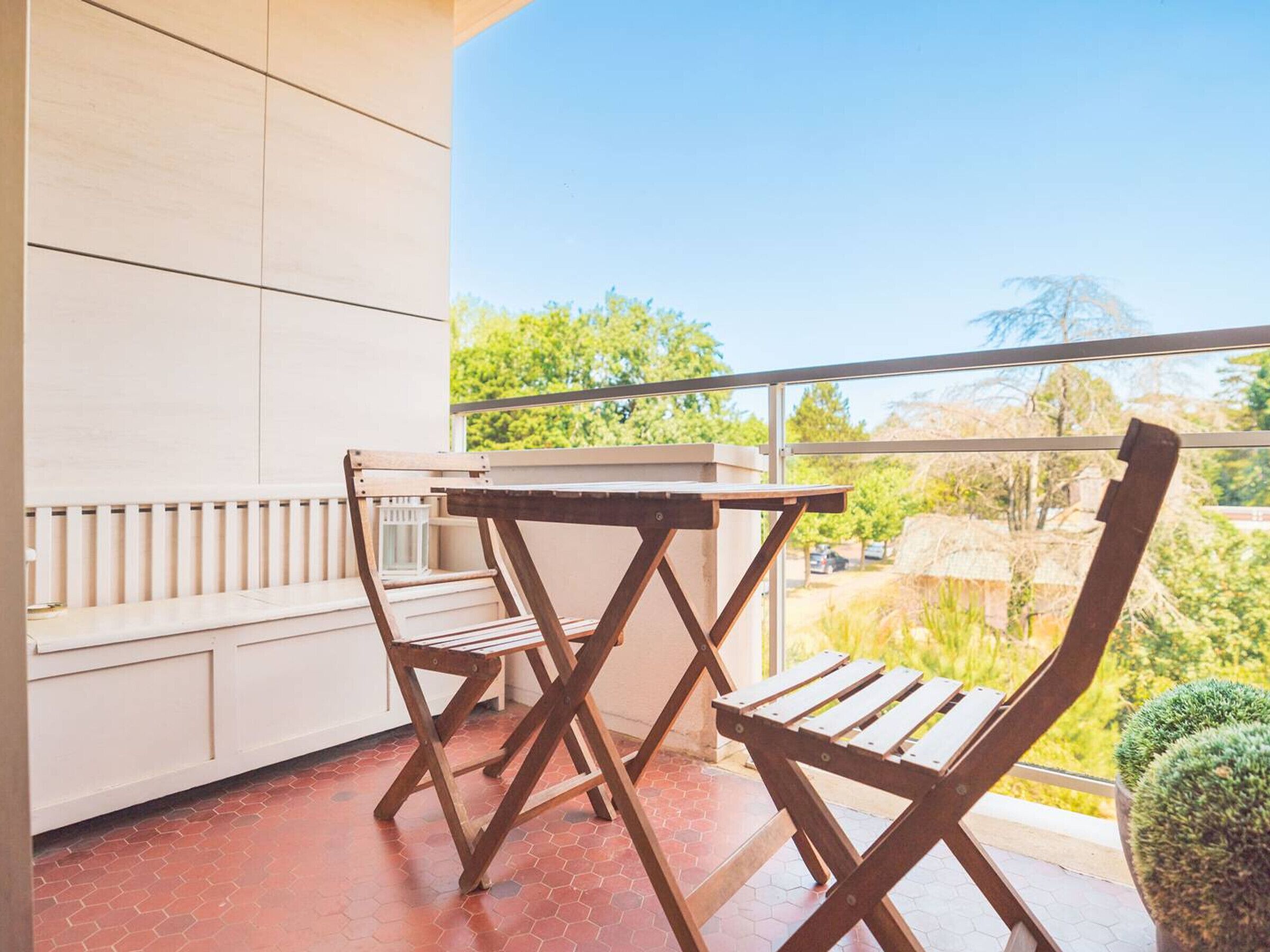 Een balkon met een houten tafel en stoelen, uitzicht op groen en een betegelde vloer.