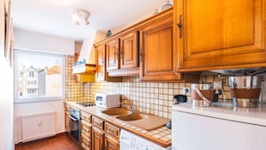 A compact kitchen with wooden cabinets, a built-in oven, a microwave, and a washing machine. - Apartment with sea side view, city center (Le Touquet-Paris-Plage)