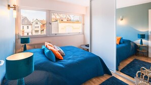 A bedroom with a large bed, a window with a view of buildings, a mirror, and a small table with a lamp. - Apartment with sea side view, city center (Le Touquet-Paris-Plage)