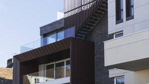 A modern multi-story building with a glass balcony, a visible staircase, and a flat roof.