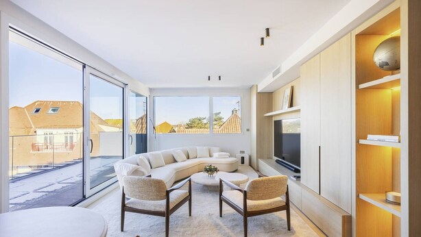 A modern living room with a curved sofa, two armchairs, a TV, and a dining area.