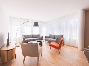 Ein modernes Wohnzimmer mit zwei grauen Sofas, einem runden Couchtisch, einem hölzernen Beistelltisch, einem roten Sessel und einer Stehlampe.