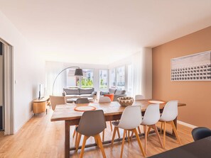 Ein moderner Essbereich mit einem Holztisch, sechs Stühlen und einem großen Fenster mit Blick ins Freie.