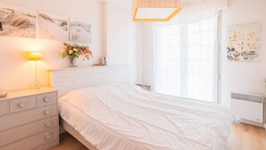 Ein Schlafzimmer mit einem Bett, einem Nachttisch mit Lampe, einem Fenster mit Vorhängen und Wandbildern.