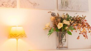 Eine Lampe mit gelbem Schirm und eine klare Vase mit Blumen auf einem Kaminbrett.