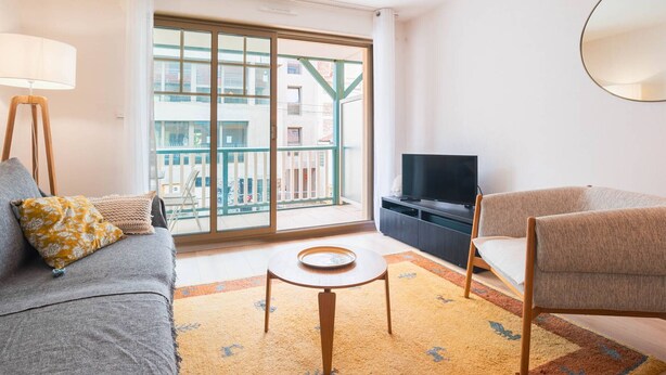 Ein modernes Wohnzimmer mit Sofa, Sessel, Fernseher und einem kleinen Tisch.