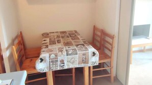 A small dining area with a table covered by a patterned tablecloth, wooden chairs, and a wooden cabinet above. - Cozy 2-room near slopes at Isola 2000 (Isola 2000)