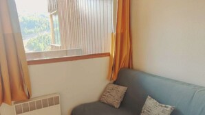 A room with a window, a radiator, and a blue sofa with two cushions. - Cozy 2-room near slopes at Isola 2000 (Isola 2000)