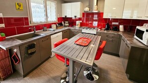 A modern kitchen with a central island, red and white cabinets, and a stainless steel sink. - Charming Stone House with Garden Near Chinon (Sazilly)