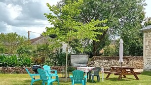 A backyard with a stone wall, a wooden table, and several chairs. - Charming Stone House with Garden Near Chinon (Sazilly)