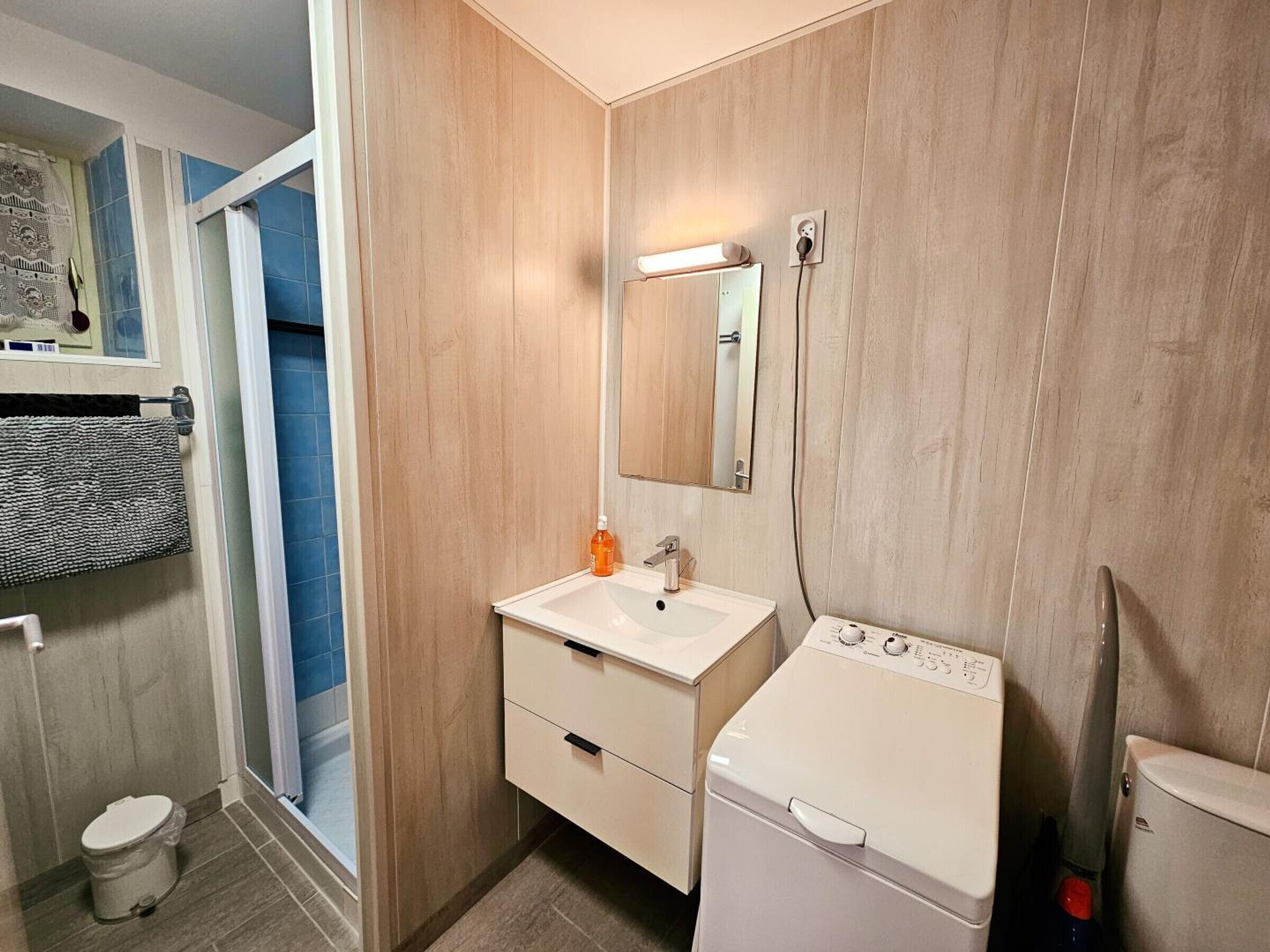 Et moderne badeværelse med en trævæg, en hvid vask, et spejl, et toilet og en vaskemaskine.