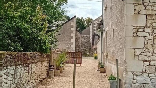 A narrow alleyway with stone walls and a gravel path leading to a wooden gate. - Charming Stone House with Garden Near Chinon (Sazilly)