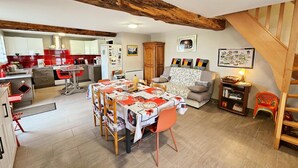 A spacious living area with a wooden ceiling, a dining table with a Hello Kitty tablecloth, a sofa, and a staircase. - Charming Stone House with Garden Near Chinon (Sazilly)