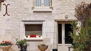 A building with a stone facade, a window with a curtain, and a door with a glass panel. There are three planters with plants in front of the building. - Charming Stone House with Garden Near Chinon (Sazilly)