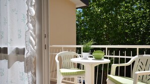 Un balcón con sillas y una mesa blancos, una planta en maceta y vistas a árboles.