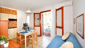Una stanza compatta con angolo cottura, zona pranzo, divano e vista sull'esterno.