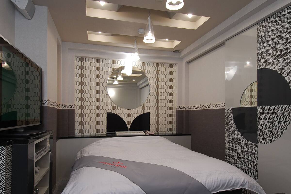 A modern hotel room with a large bed, a television, a ceiling light, and a patterned wall.