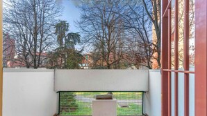 A balcony with a concrete planter, a metal fence, and a view of trees and buildings. - Moncler House Navigli (Milano)