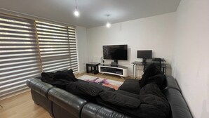 Una sala de estar moderna con un sofá de cuero negro, un televisor de pantalla plana y una pequeña mesita auxiliar.