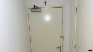 Un pasillo estrecho con suelo de madera, una puerta blanca con una cruz pequeña en la parte superior y un picaporte a la derecha.