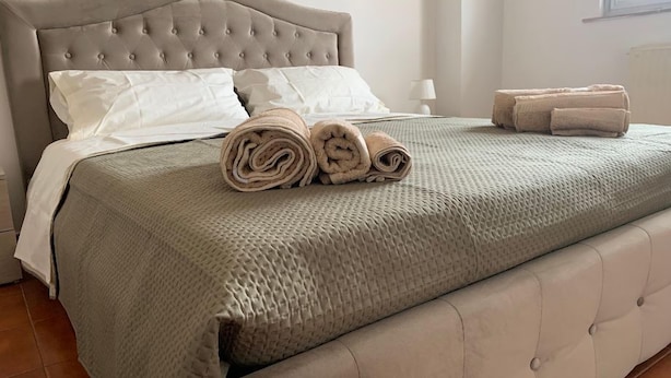 A neatly made bed with a grey quilt, rolled towels, and a tufted headboard in a hotel room. - George Penthouse Palermo (Palermo)