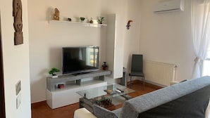 A living room with a flat-screen TV on a white entertainment unit, a glass coffee table, a grey sofa, and a radiator. - George Penthouse Palermo (Palermo)