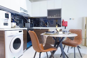 A modern kitchen with a built-in washing machine, a dining area with two chairs, and a fire extinguisher on the wall. - Bloomfields Studio - Jewelz bu Danube - Arjan (Dubai)
