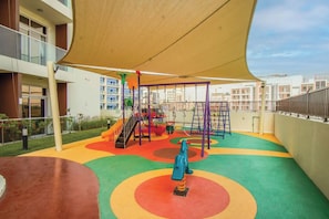 A children's play area with a slide, climbing structures, and colorful ground markings. - Bloomfields Studio - Jewelz bu Danube - Arjan (Dubai)