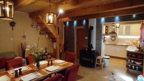 Un comedor acogedor con una mesa de madera dispuesta para cuatro, una chimenea y una cocina al fondo.