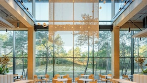 A modern dining area with large windows, wooden tables and chairs, and a central hanging light fixture. - Shellter Hotel Resort & Spa (Trzebiatow)